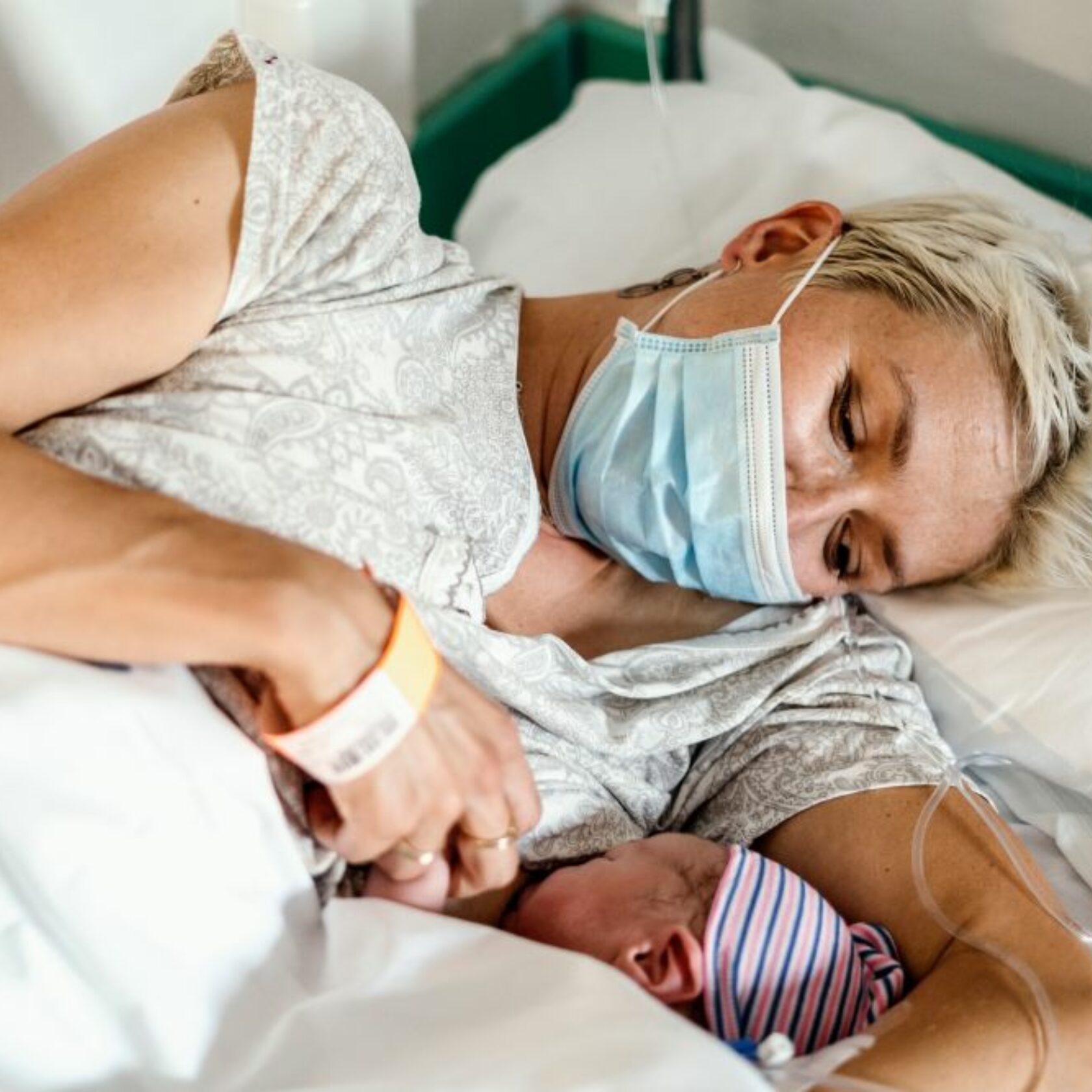 Geburt während der Pandemie - junge Mutter stillt ihr Neugeborenes mit Mundschutz