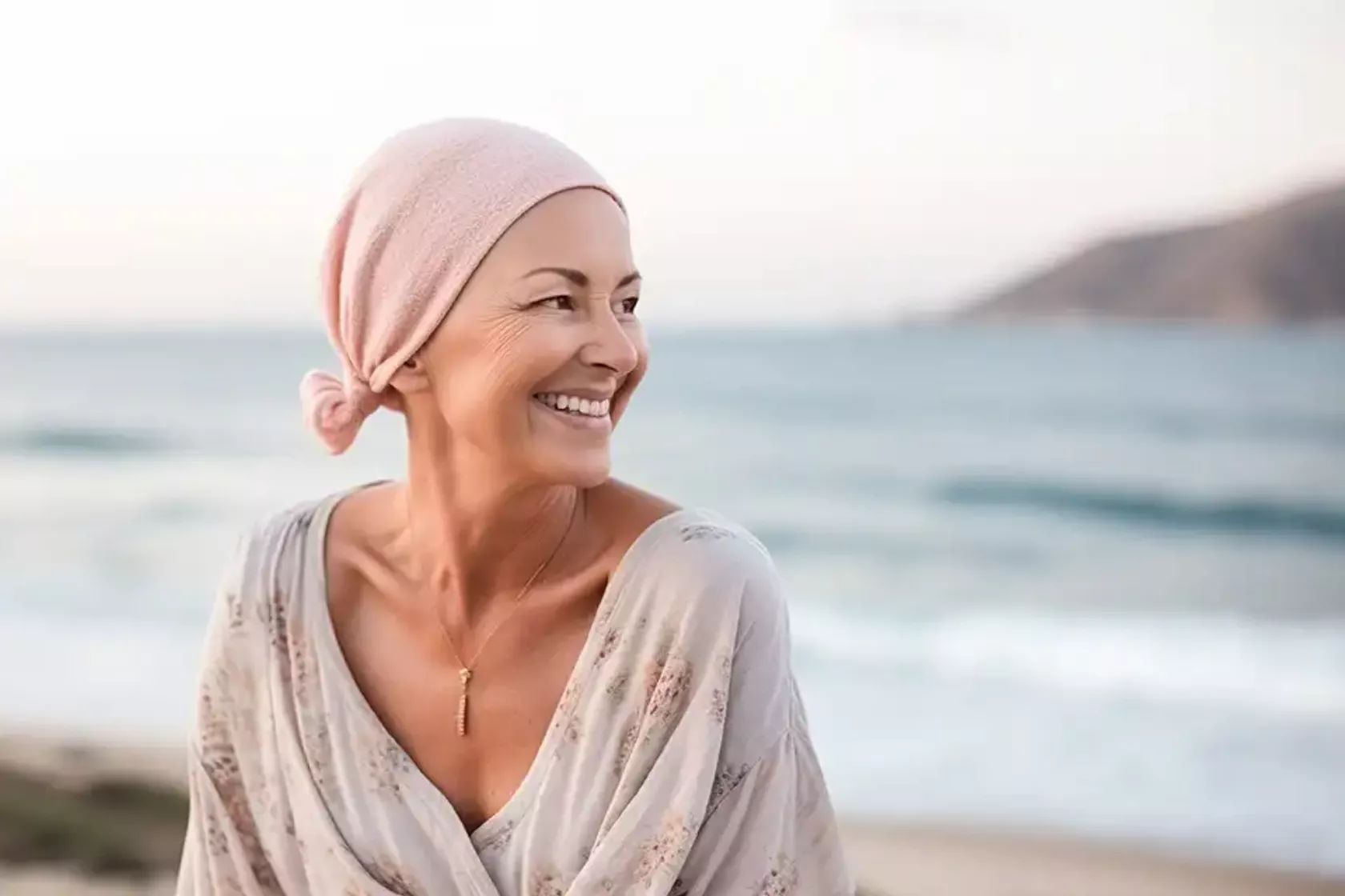 Frau mit Kopftuch am Strand lächelt.