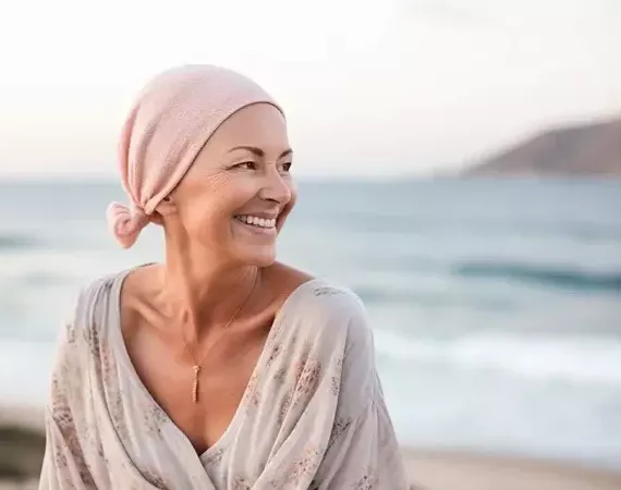 Frau mit Kopftuch am Strand lächelt.