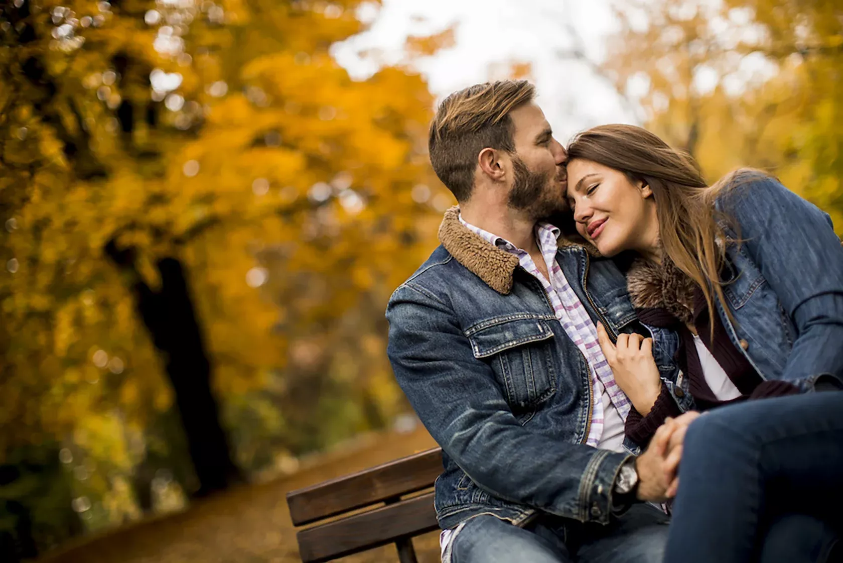 Junges Paar sitzt auf einer Parkbank umarmt sich glücklich und findet Entspannung beieinander.