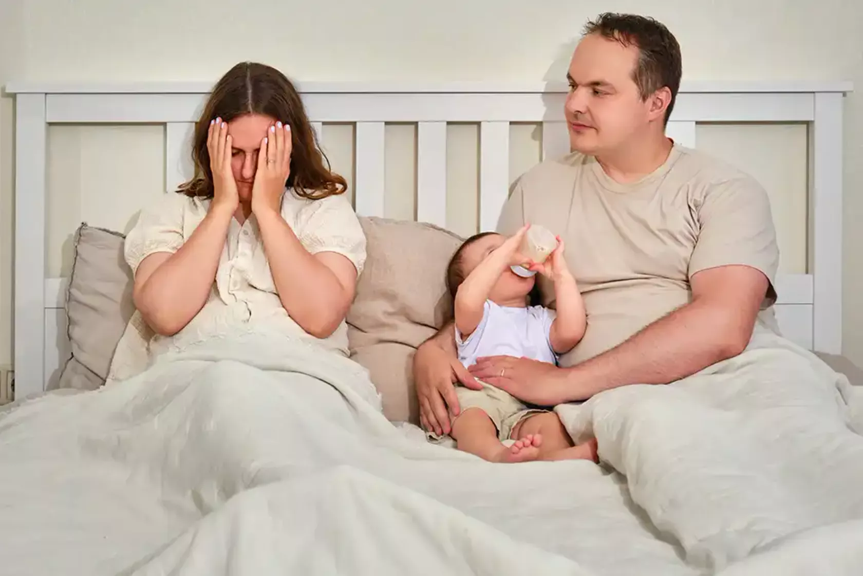 Paar mit Baby sitzt im Bett, die Frau weint - Wochenbettdepression.
