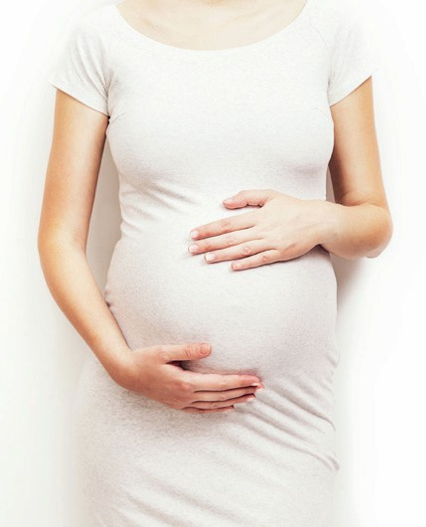 Frontalansicht einer Schwangeren, die ihren Bauch hält, man sieht das Gesicht nicht.