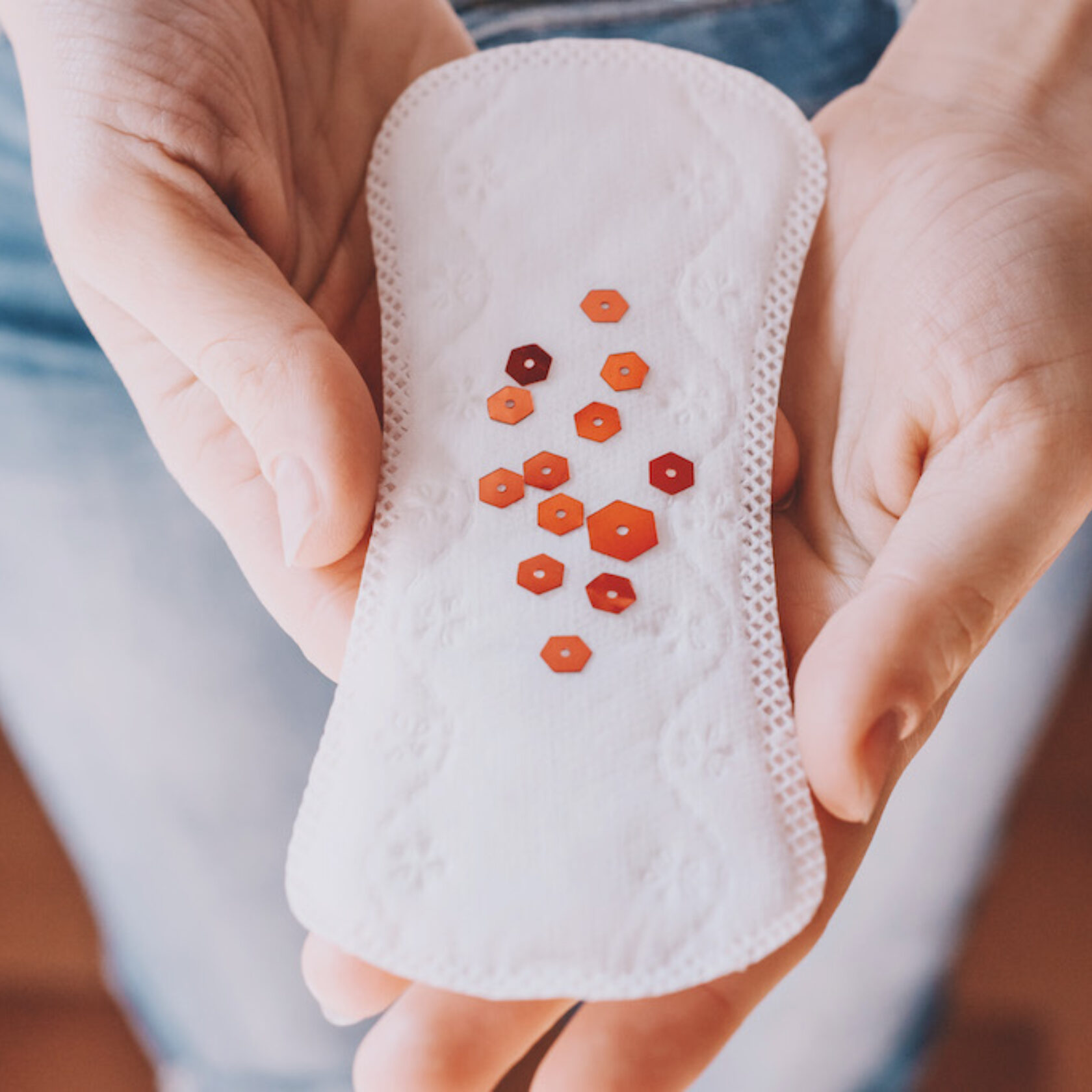 Eine Slipeinlage mit daraufgestreuten roten Partikeln als Symbol für die Menstruationsblutung