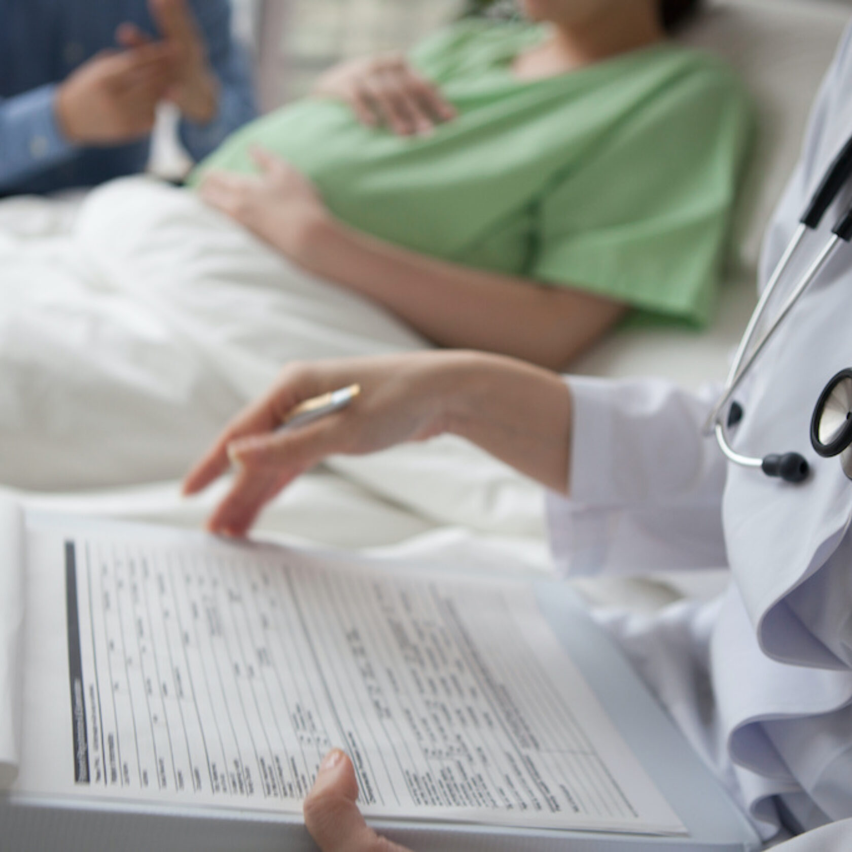 Im Krankenhaus Ärztin am Bett einer Frau nach dem Kaiserschnitt. Sie notiert etwas in der Patientenakte.