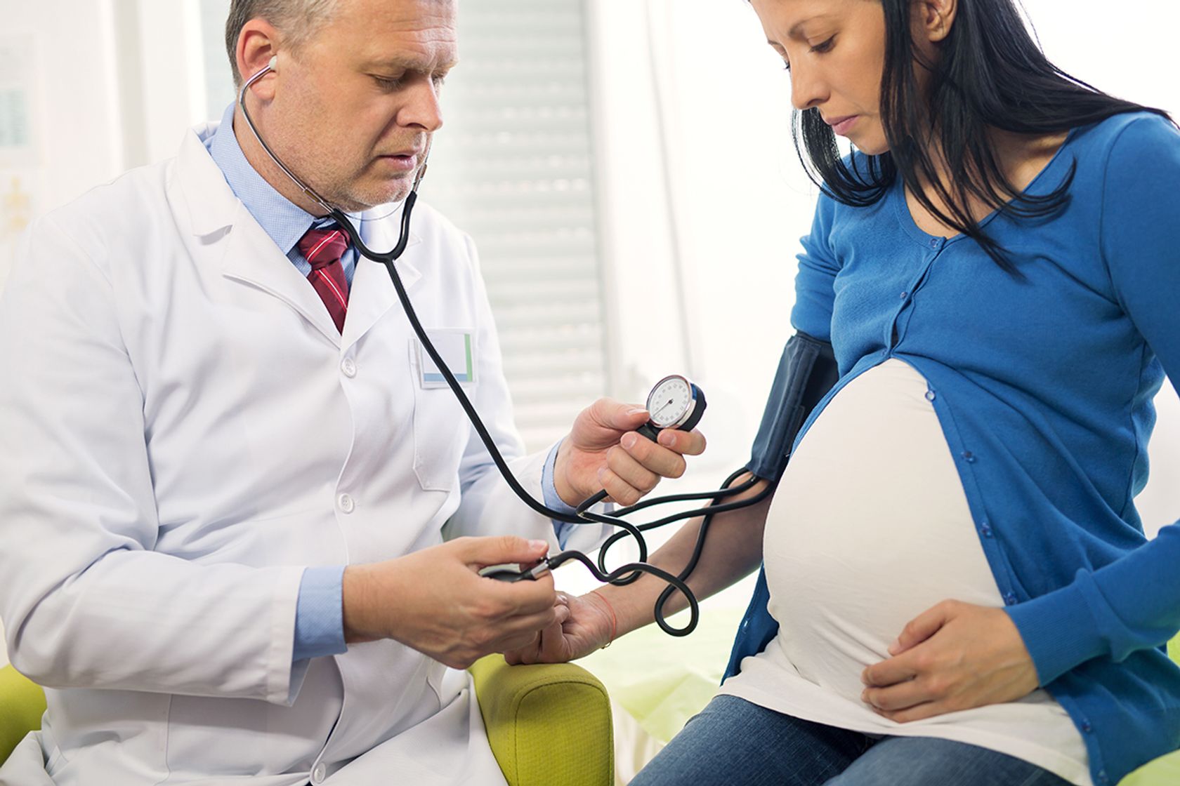 Arzt misst bei einer Hochschwangeren den Blutdruck.