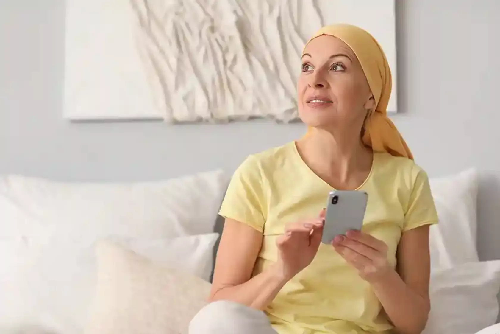 Krebspatientin mit Kopftuch mit Smartphone in der Hand denkt nach.