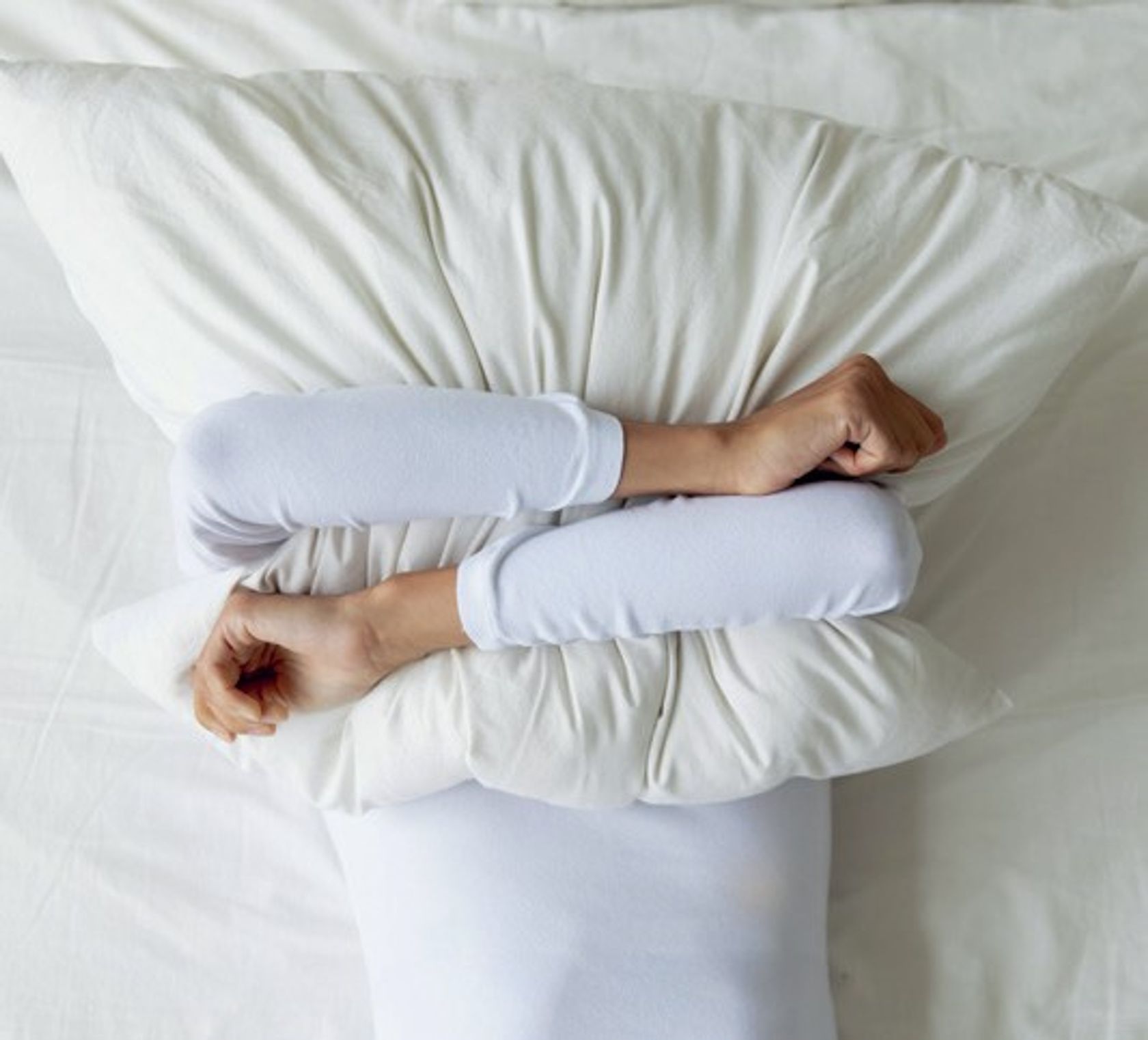 Eine Person liegt im Bett und umarmt das Kopfkissen, sodass man den Kopf nicht sehen kann.