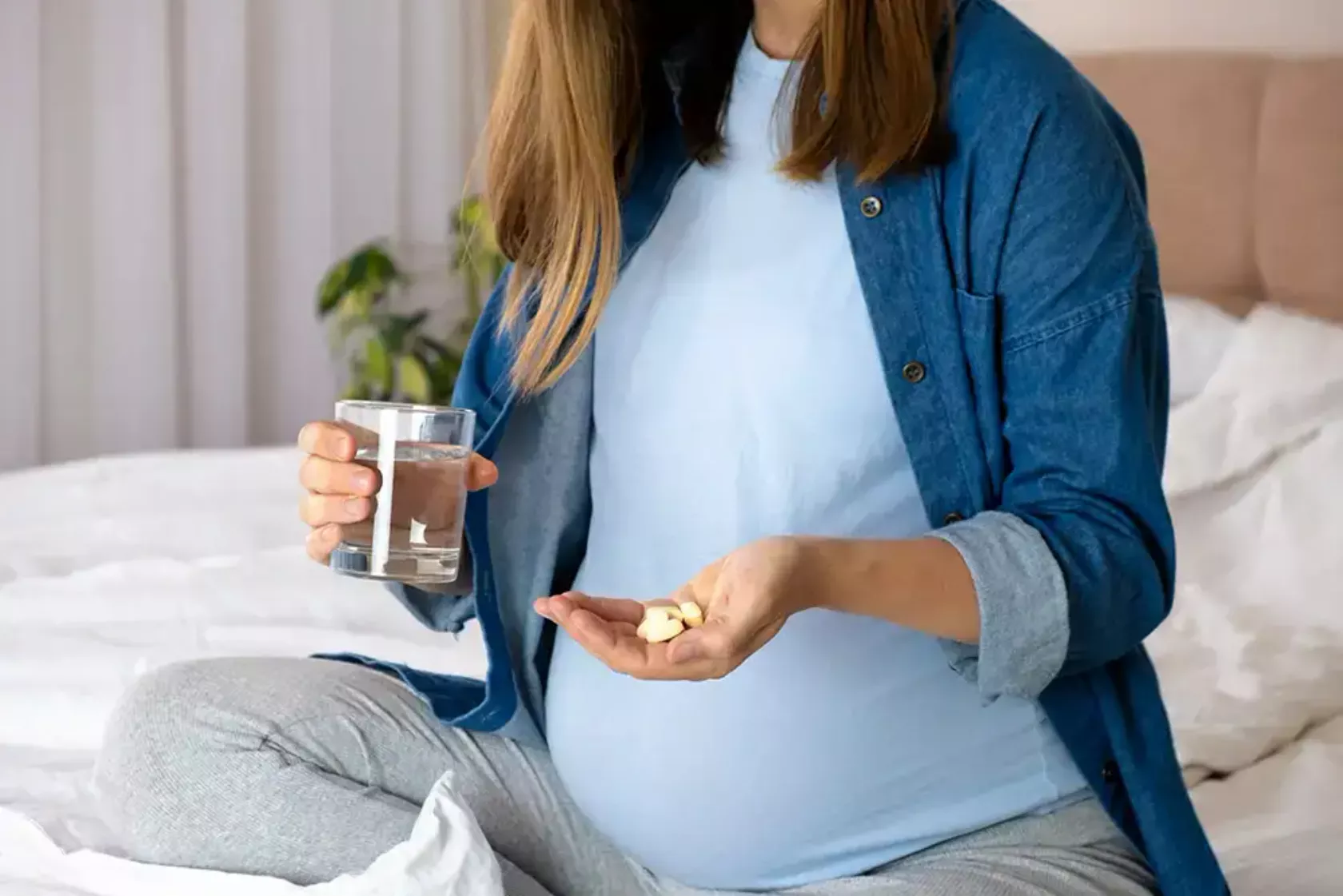 Schwangere hält ein Glas Wasser und Tabletten in der anderen Hand.