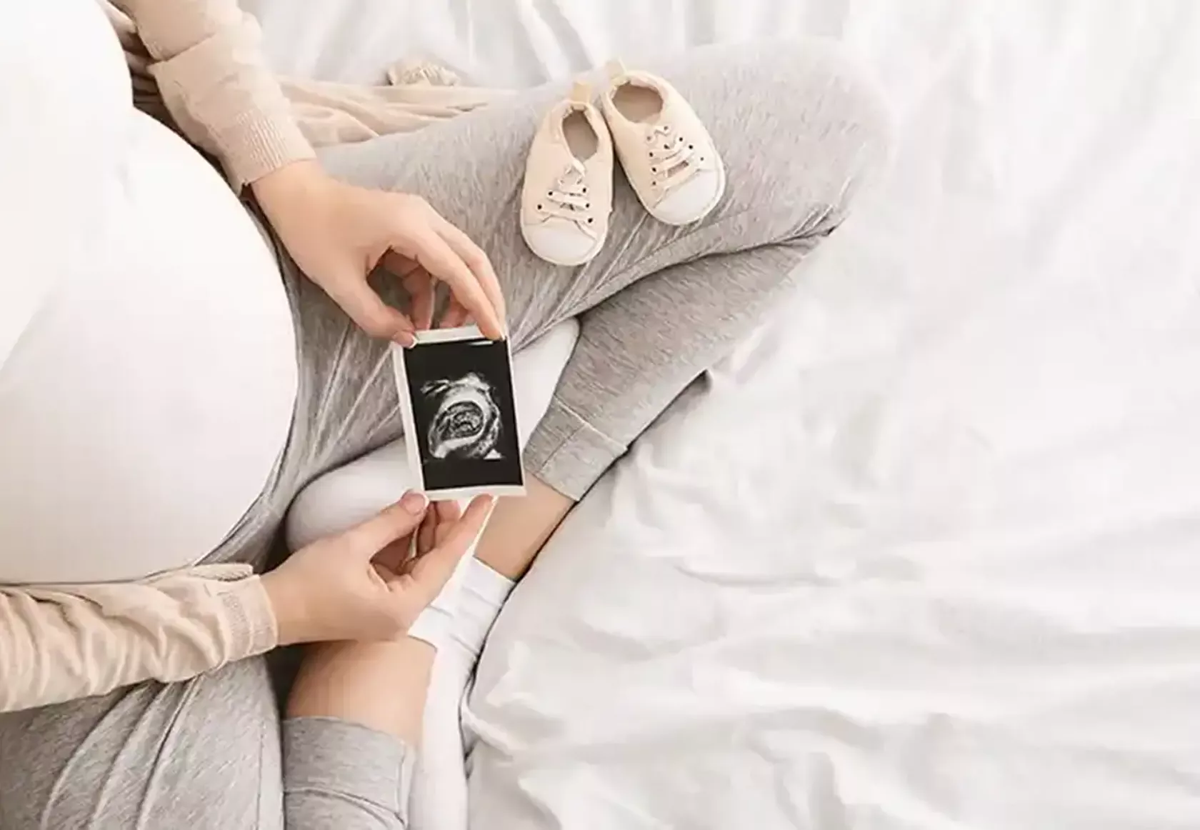 Blick von oben auf eine hochschwangere Frau, die ein Ultraschall-Bild in den Händen hält und betrachtet.